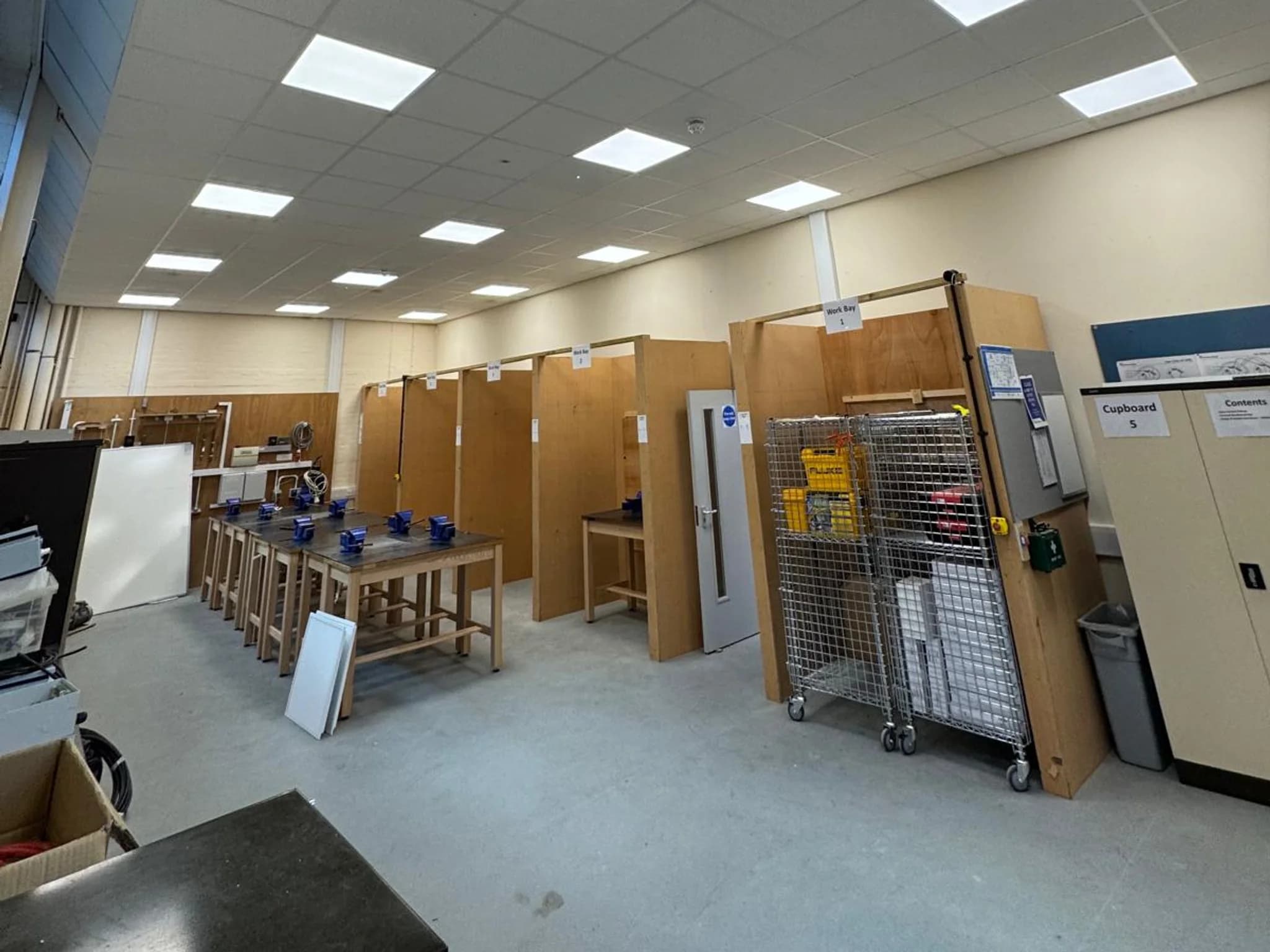 A college training workshop with a grid of lit LED panels in the suspended ceiling above numbered work bays